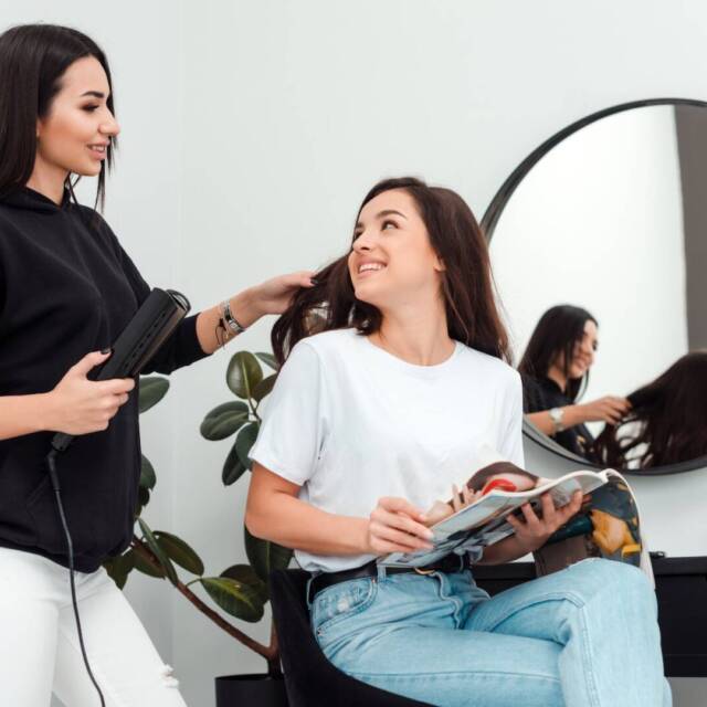 Happy woman hairdresser doing hairstyle for young girl